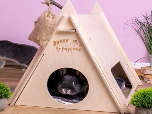 Sød kanin gemmer sig i et træhus fra mærket Bunny by Puppijames, designet til gnavere. Huset har en trekantet form med åbninger, der giver et hyggeligt og sikkert tilholdssted til mindre kæledyr.
